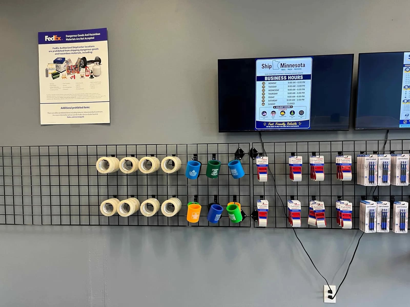 Packing tape, tape guns and koozies on display below the business hours screen at Ship Minnesota